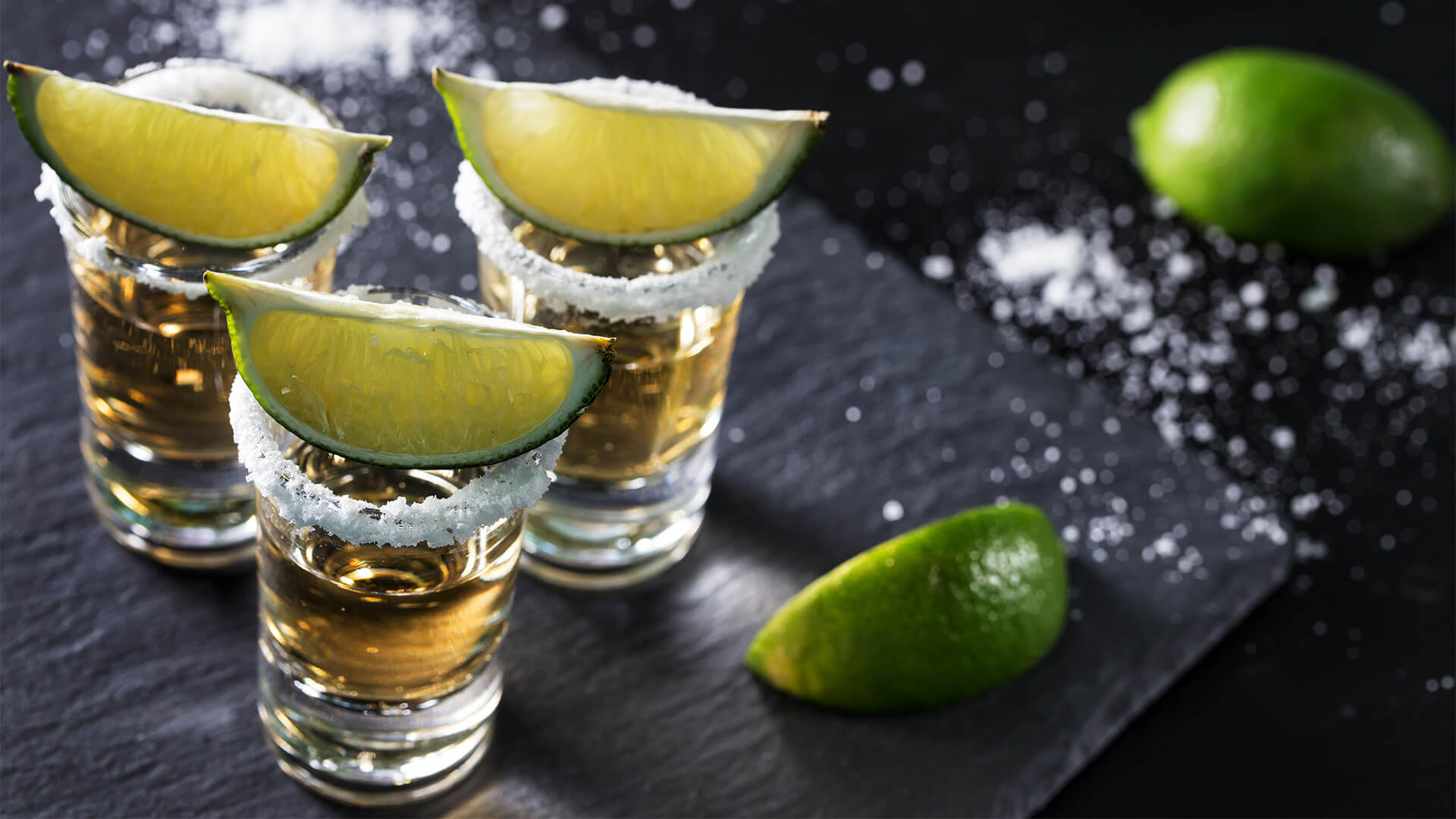 Shot glasses of tequila with lime wedges and salt on the rim