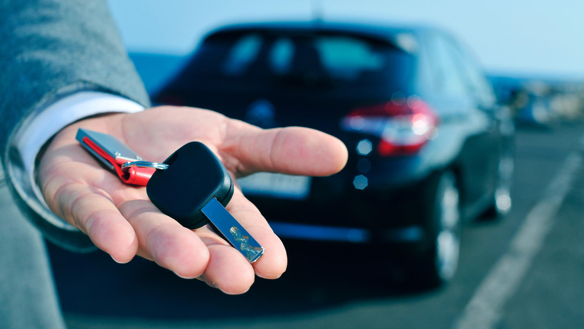 Someone holding the keys to a company car. The car in out of focus in the background