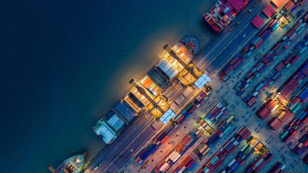 Bird's eye view of a dock with shoipping containers and cargo ships docked in the evening