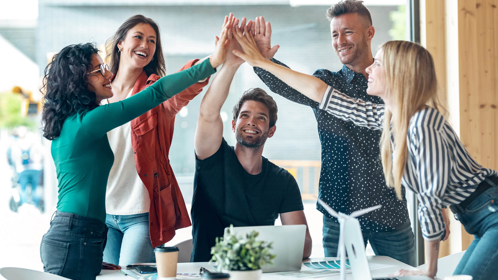 Group of successful smart business team celebrating good job while holding up their right hands on coworking place