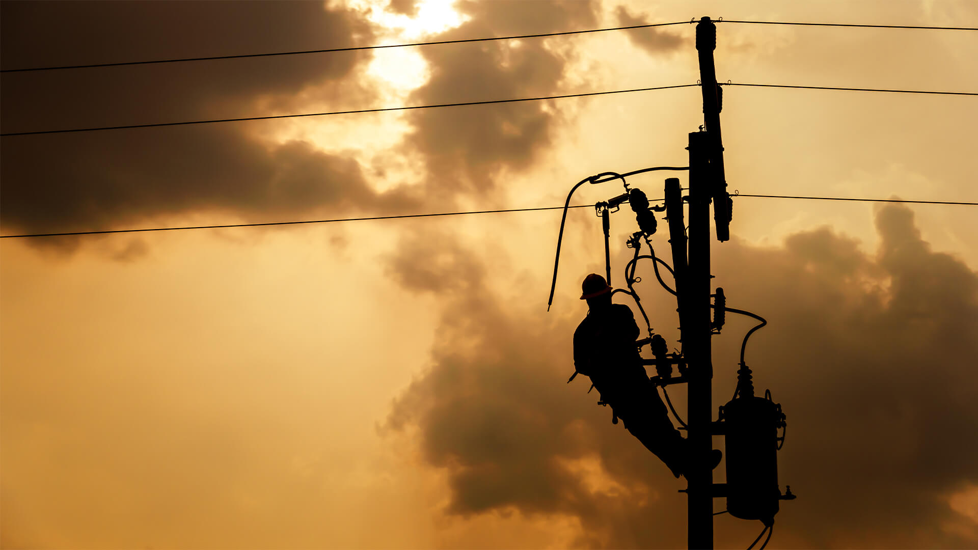 The silhouette of power lineman climbing on an electric pole with a transformer installed