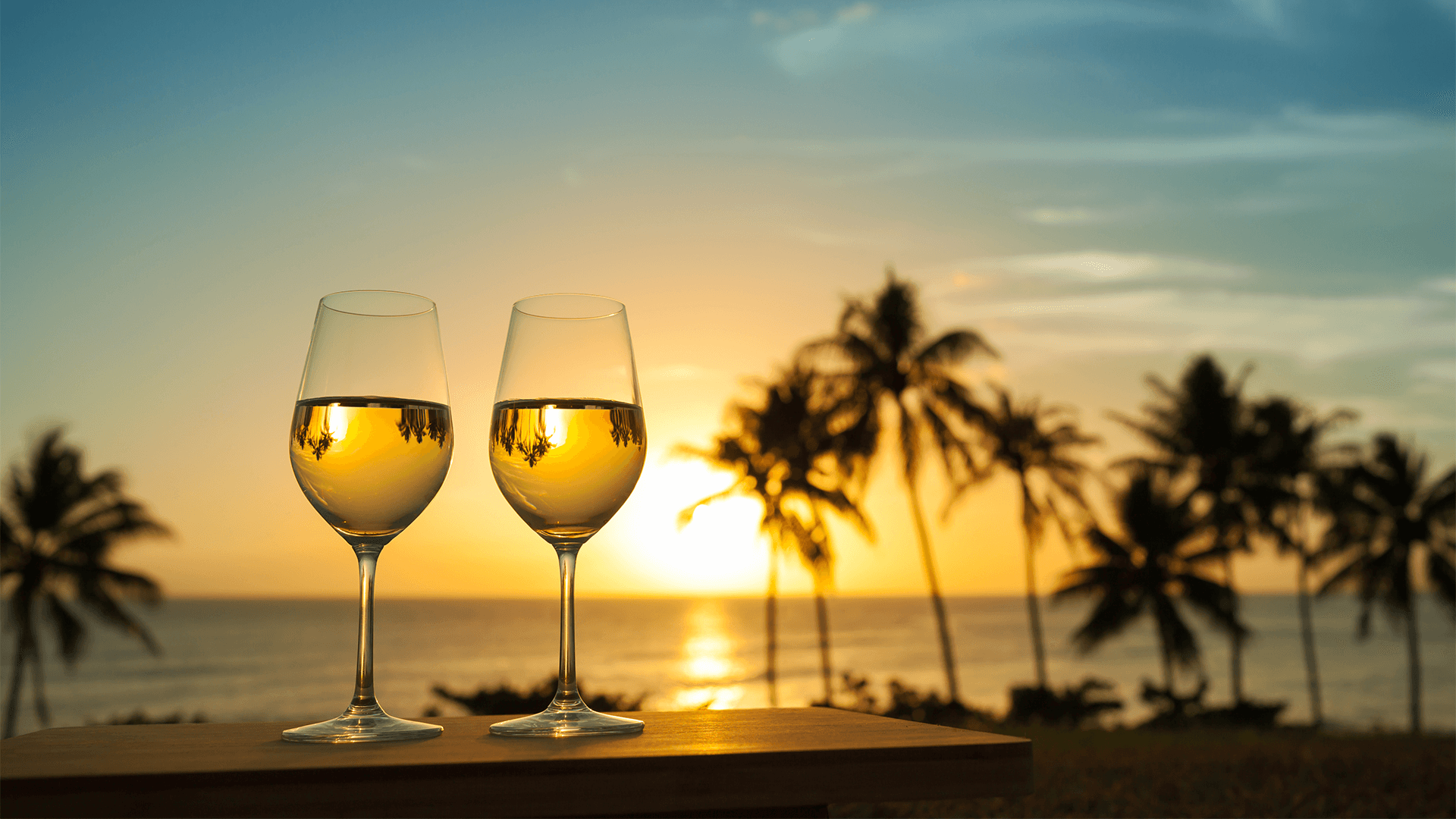 Wine glasses on a table with palm trees in the background