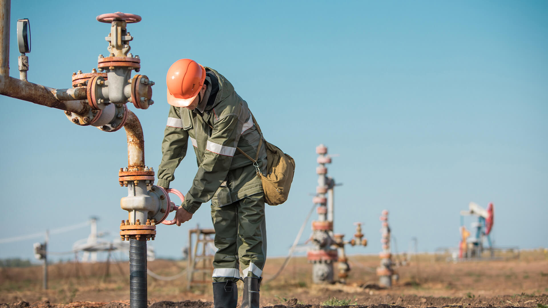 Oil worker is turning valve on the oil pipeline, oil deposit on the background.